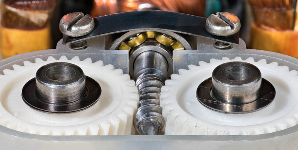 Close-up of a mechanical assembly featuring a metal worm gear meshing with two white plastic spur gears, secured with metal components.
