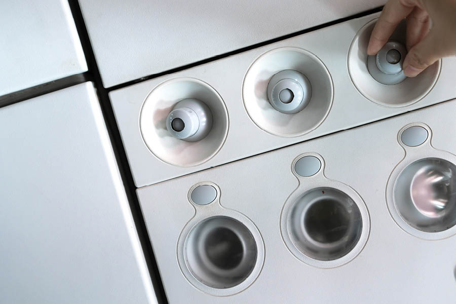 A hand adjusts one of several round dials on a white control panel with metallic circular slots below.