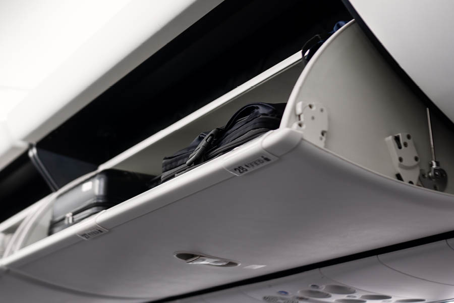 Open airplane overhead compartment with black suitcases stored inside. The label "28 A" is visible on the compartment.