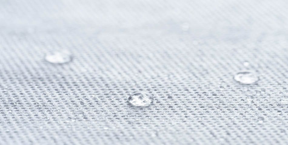 Close-up of water droplets on a textured, light gray fabric surface.