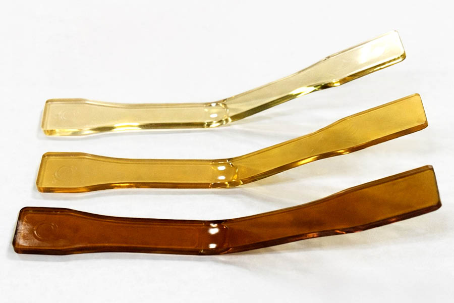 Three transparent plastic samples in varying shades of brown and yellow are arranged parallel on a white background.