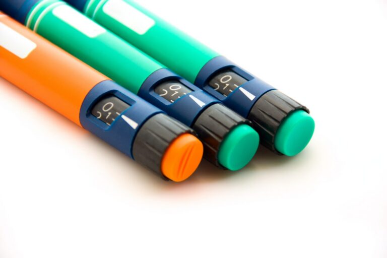 Three insulin pens with digital dose displays and medical-grade polymer design are shown on a white background, each with different colored bodies and caps: orange, turquoise, and green.