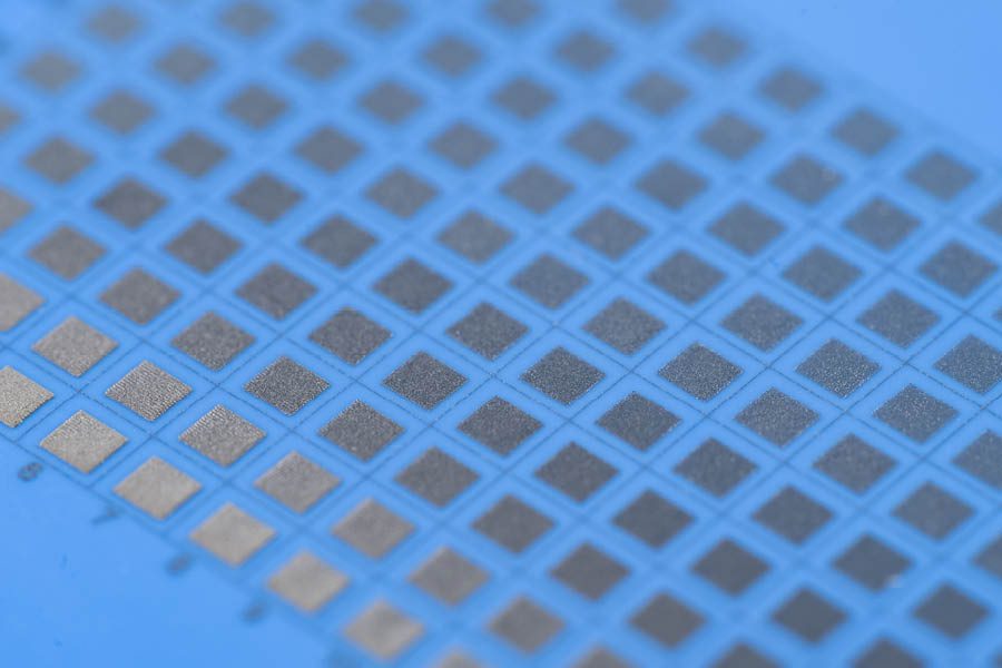 Close-up view of an array of metallic square microchips or sensors arranged in a grid pattern on a blue surface.