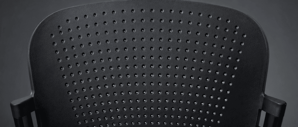 Close-up of the backrest of a black plastic chair with a pattern of small, evenly spaced circular holes.