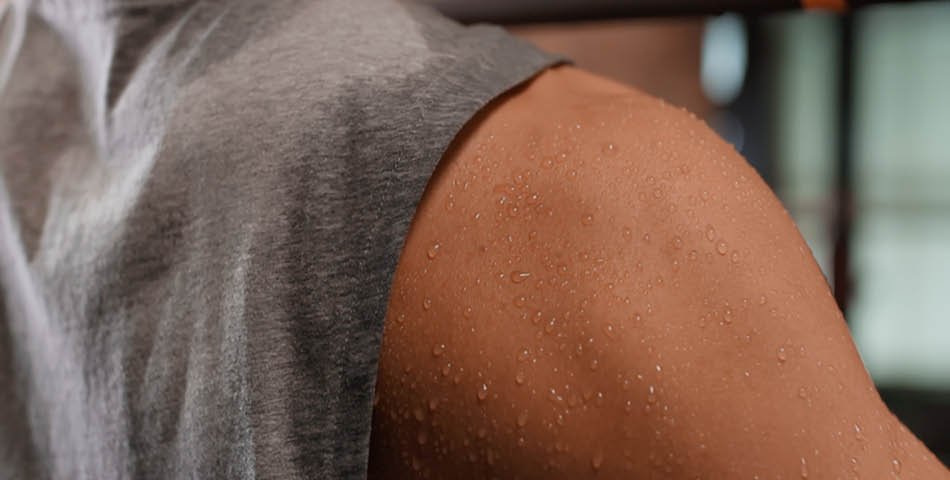 Close-up of a person’s shoulder and upper arm covered in sweat, with part of a gray sleeveless shirt visible.