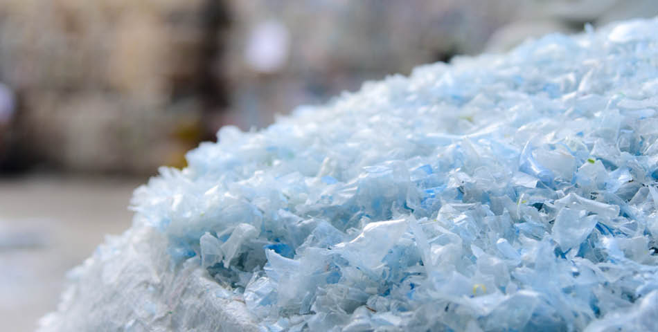 A close-up of a large pile of shredded translucent plastic pieces, likely prepared for recycling, with a blurred background.