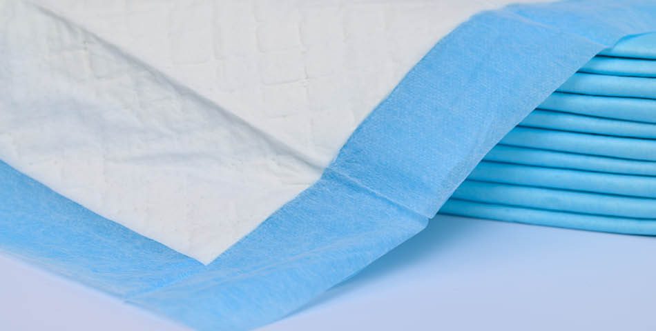 A stack of disposable absorbent pads with white centers and blue edges, arranged neatly on a flat surface.