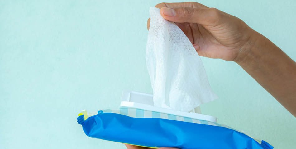 A hand pulls a single wet wipe from an open blue package against a light background.