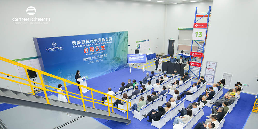 People seated in an audience at an opening ceremony for an Americhem clean compounding facility, with a speaker at a podium on stage.